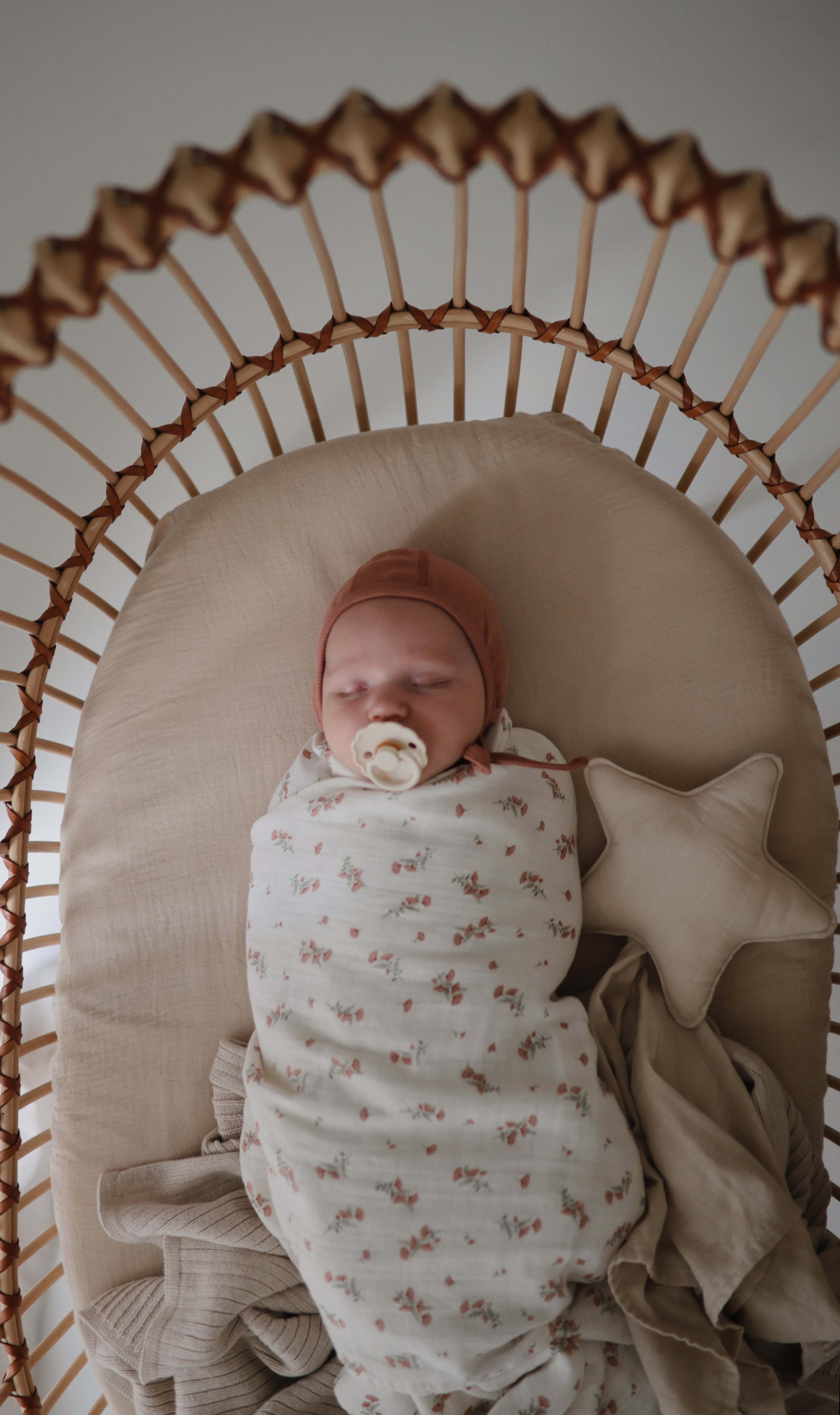 Newborn baby wrapped in a floral blanket with a pacifier from the Frigg 4-pack pacifiers in latex in Snowflake dream, lying in a wicker crib.