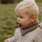 Child with a pacifier from the FRIGG 6-pack Latex Earty Wonder set wearing a brown sweater in an outdoor setting