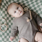 Baby in a gray onesie with a pacifier from Frigg 6-pack pacifiers in latex in Cinnamon charm on a green and white checkered blanket