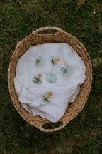 Basket with a white cloth and pacifiers from the Frigg Daisy Bloom 2-pack in silicone in Little darling cream on a grassy background