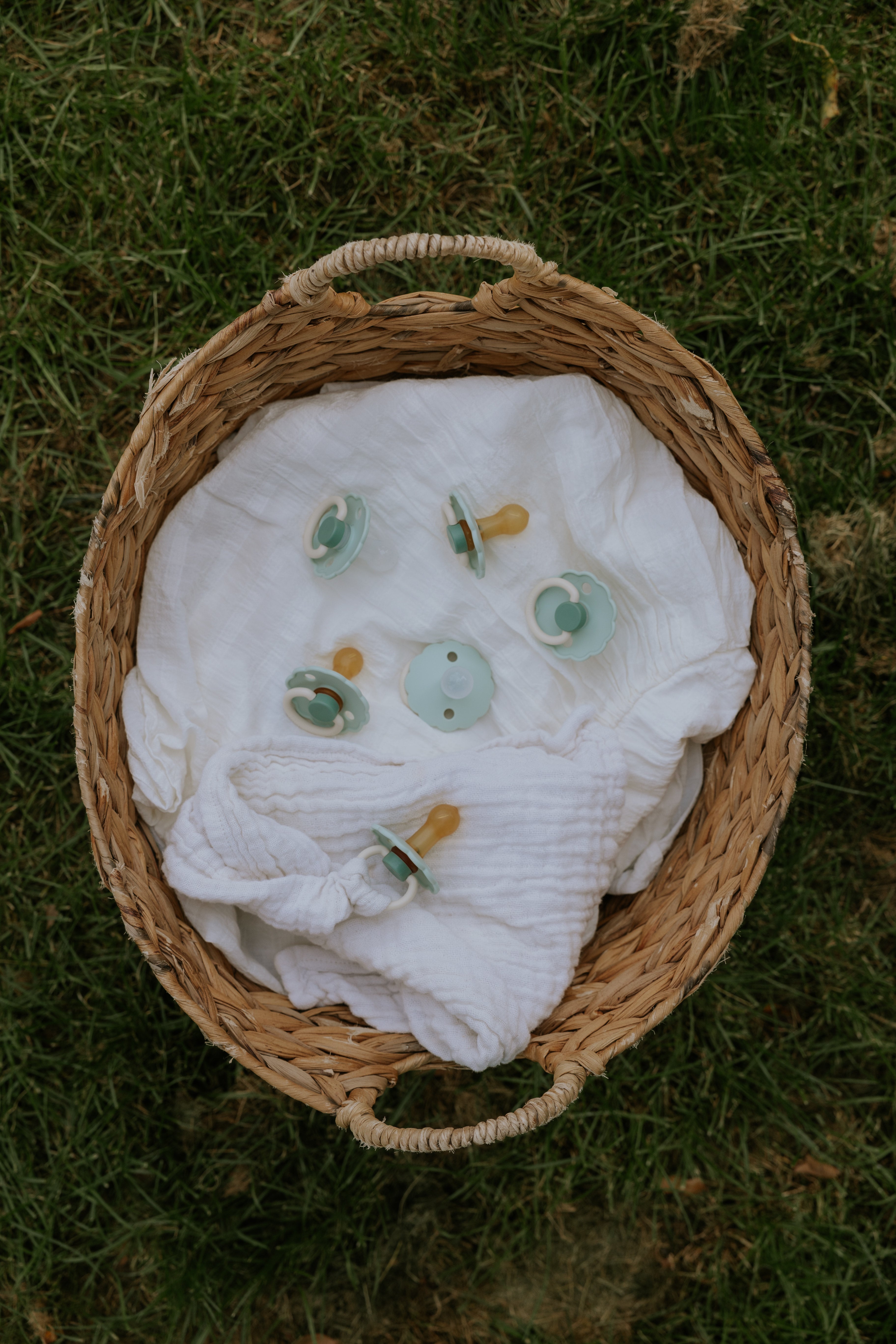Basket with a white cloth and pacifiers from the Frigg Daisy Bloom 2-pack in silicone in Little darling cream on a grassy background