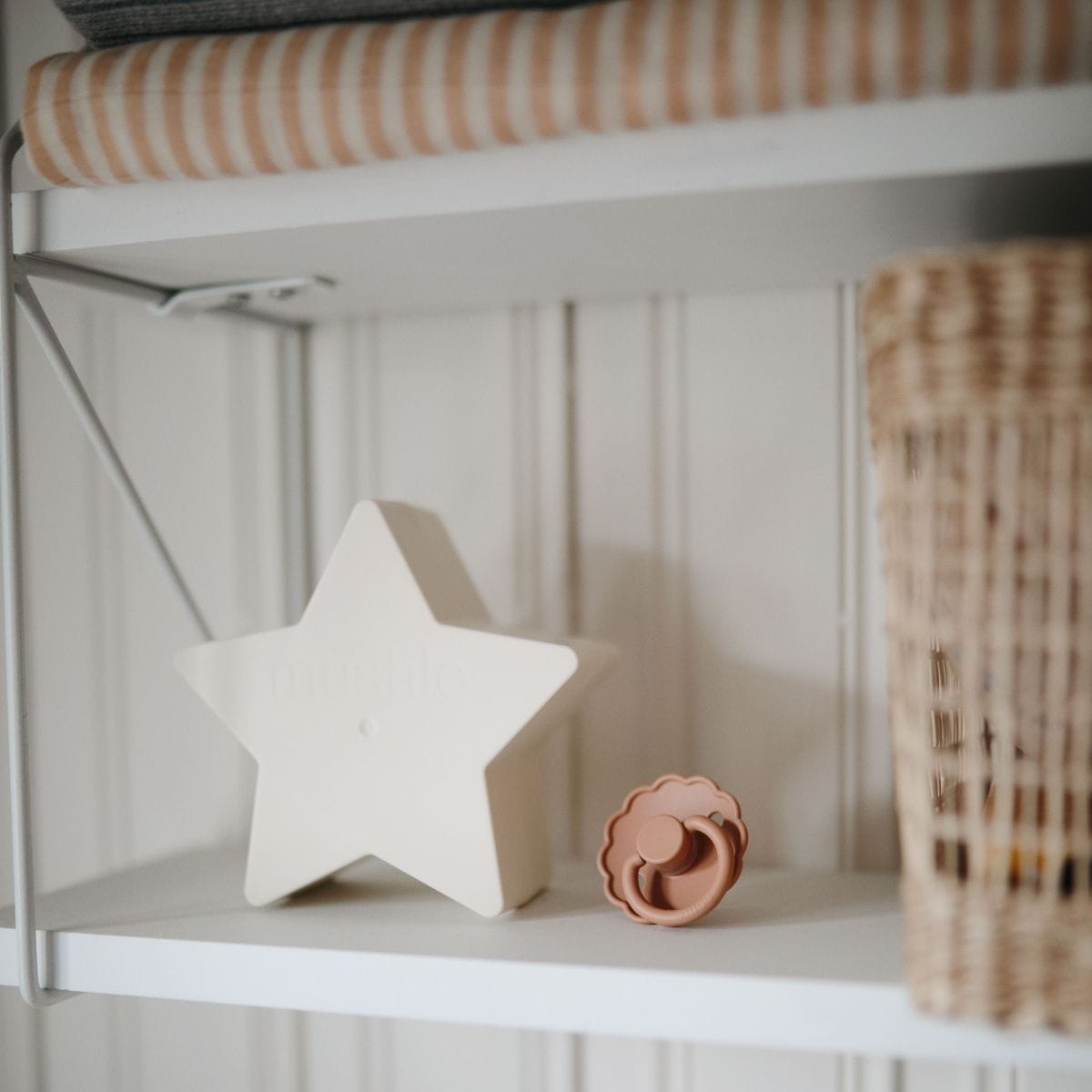 Frigg Daisy pacifier T1 2-pack in latex in Blush cream styled in a cabinet with a decorative white star