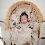 Baby lying in a basket on beige sheets with a pacifier from the Frigg Daisy 2-pack in latex in Blush cream