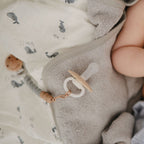 Close-up of a pacifier from the Frigg Daisy Night 2-pack in silicone in Cream croissant on grey and whale-patterned fabrics
