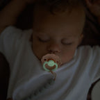 Baby sleeping with a pacifier from the Frigg Daisy Night 2-pack in silicone in Cream croissant glowing in the dark