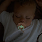 Baby sleeping with a pacifier from the Frigg Daisy pacifier 2-pack in silicone in Powder blush pink cream glowing in the dark