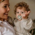 Woman holding a baby with a pacifier from the Frigg Rope Night pacifier 2-pack in latex in Stone blue sage