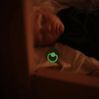 Child laying down with a Frigg Rope Night pacifier 2-pack in latex in Stone blue sage glowing in the dark