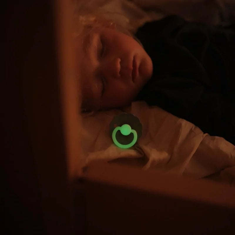 Child laying down with a Frigg Rope Night pacifier 2-pack in latex in Stone blue sage glowing in the dark