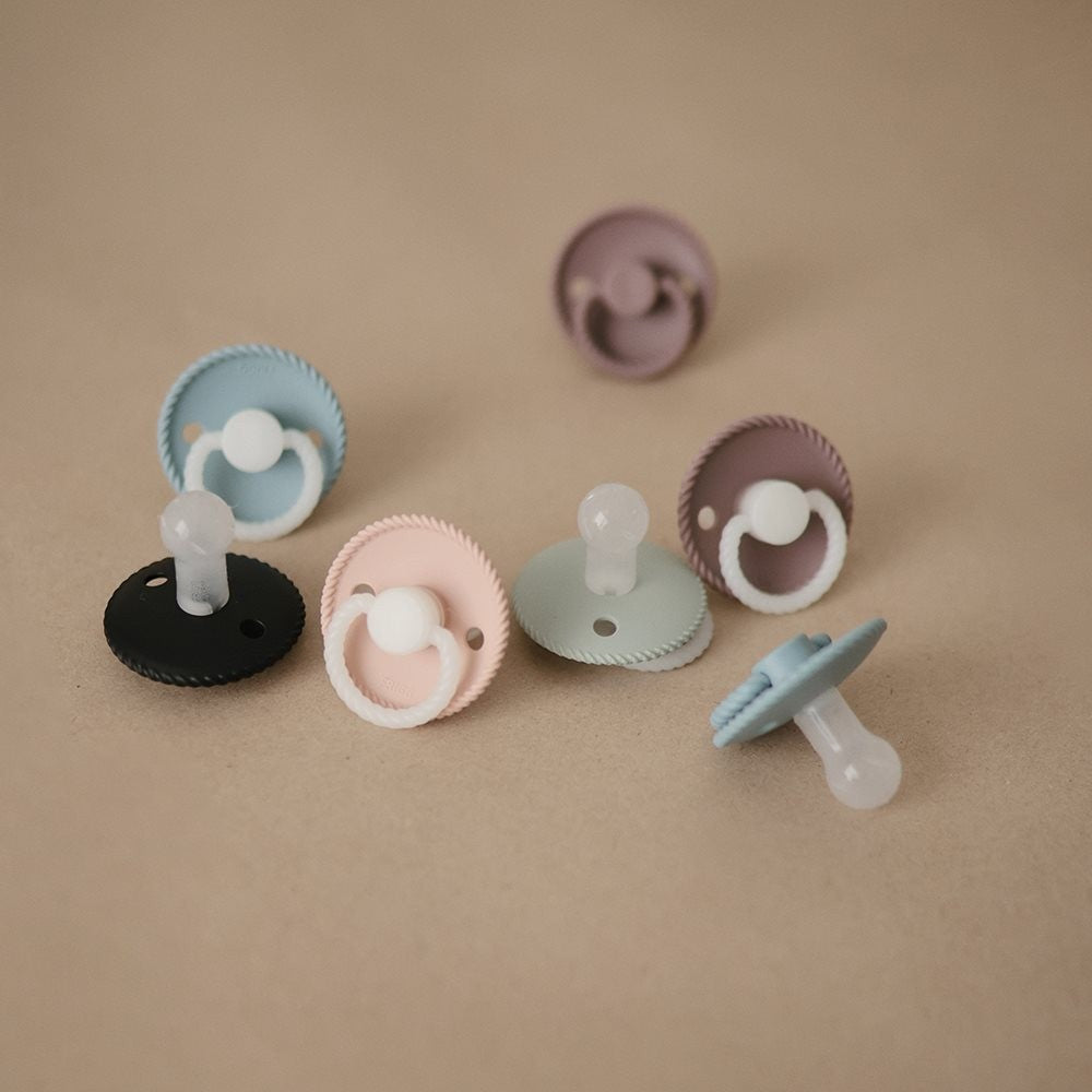 Set of colorful FRIGG Rope Night pacifiers on a beige background