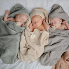 Three newborn babies wrapped in towels on a white surface with pacifiers from the Frigg Rope pacifier 2-pack in silicone in Blush croissant