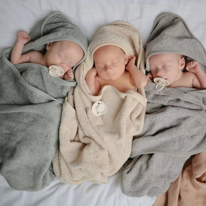 Three newborn babies wrapped in towels on a white surface with pacifiers from the Frigg Rope pacifier 2-pack in silicone in Blush croissant