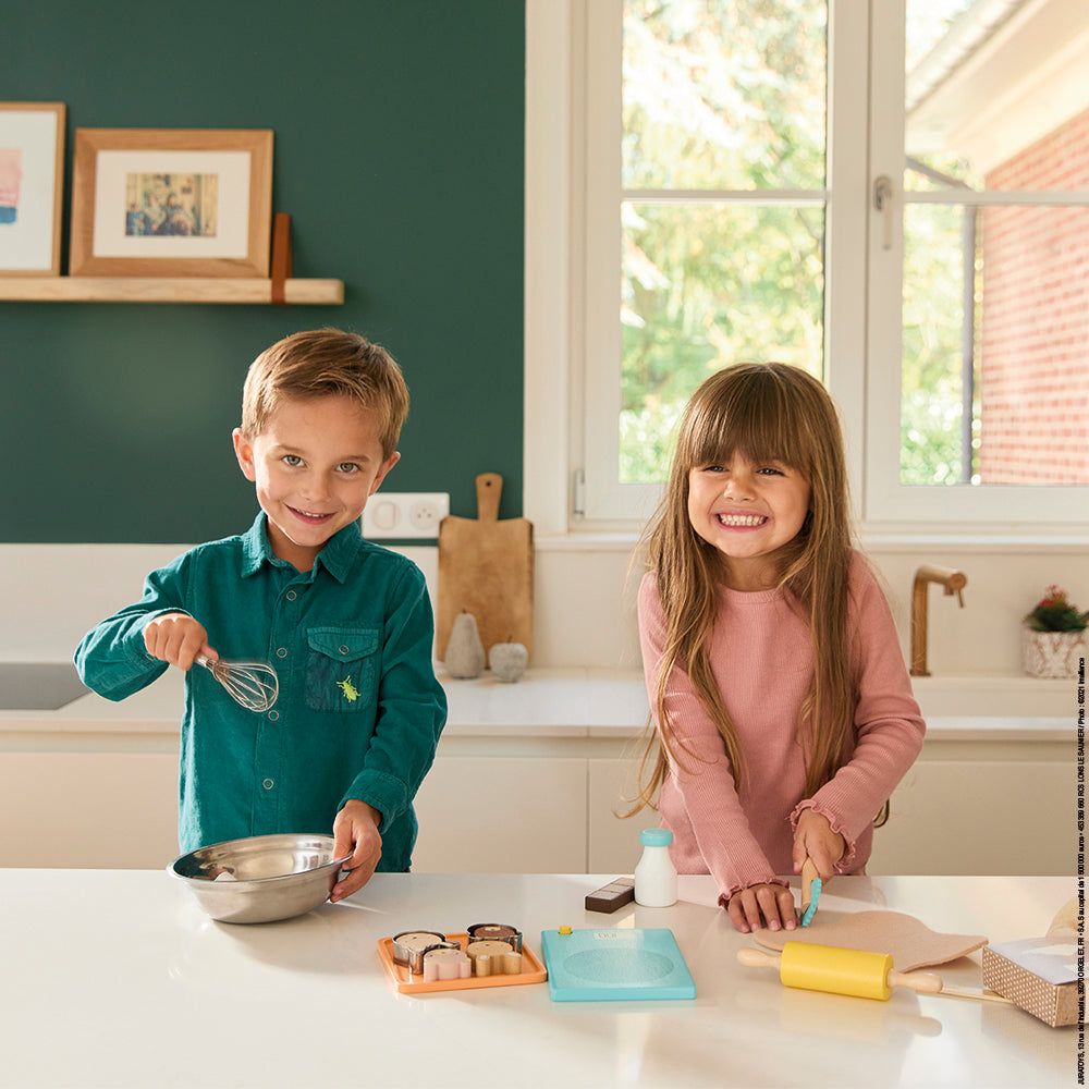 Two children in a kitchen setting playing with Janod's my pastry workshop wooden play set