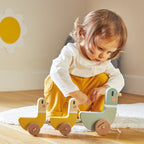Child playing with a Janod's wooden ducks on a rug in a room with a sunflower decoration on the wall