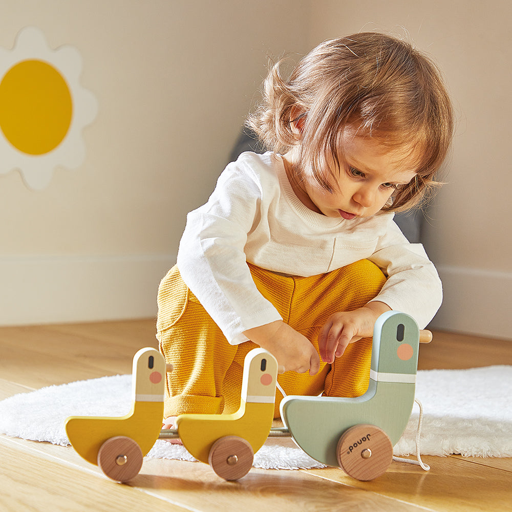 Child playing with a Janod's wooden ducks on a rug in a room with a sunflower decoration on the wall