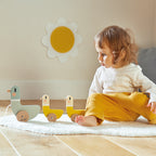 Child playing with a Janod's wooden ducks on a rug in a room with a sunflower decoration on the wall