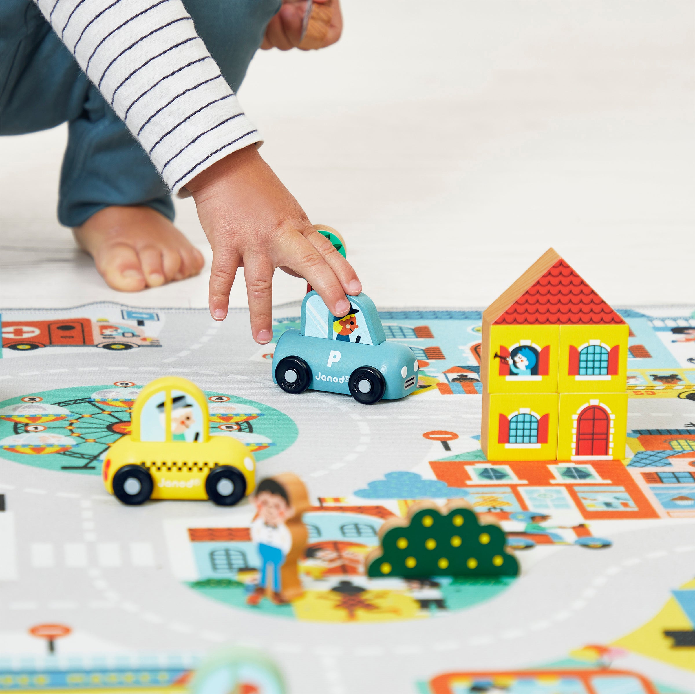 Child playing with Janod wooden police car toy and other wooden figures (not included) on a colorful play mat