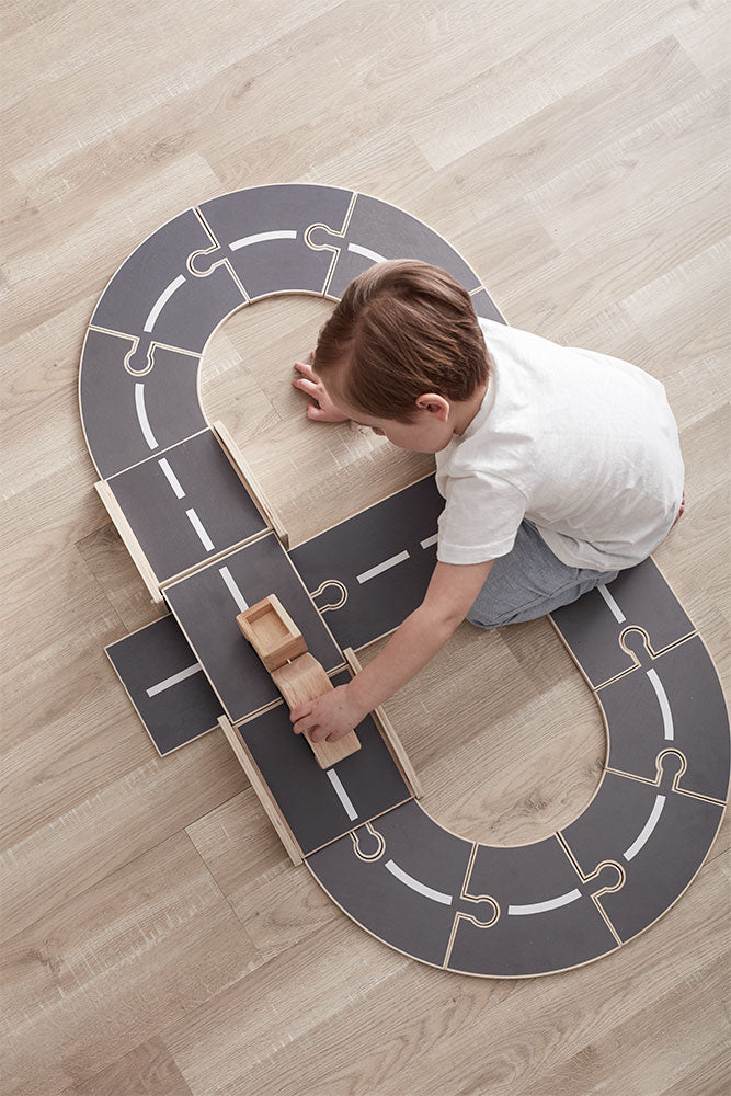 Child playing with a Kids Concept wooden car track set on a wooden floor