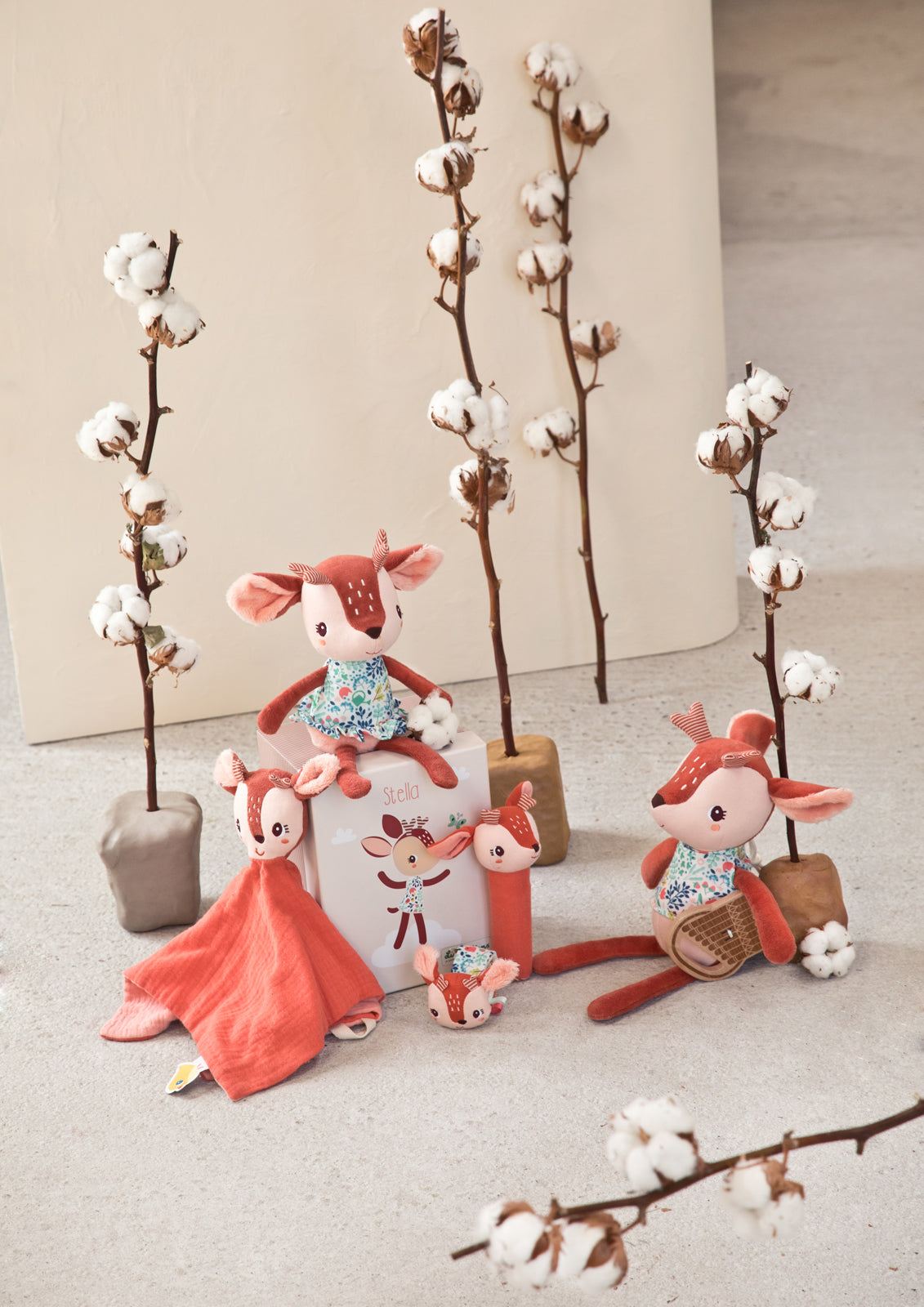 Lilliputiens Stella the Fawn squeeky rattle toy styled with other toys and decorative cotton branches on a neutral background