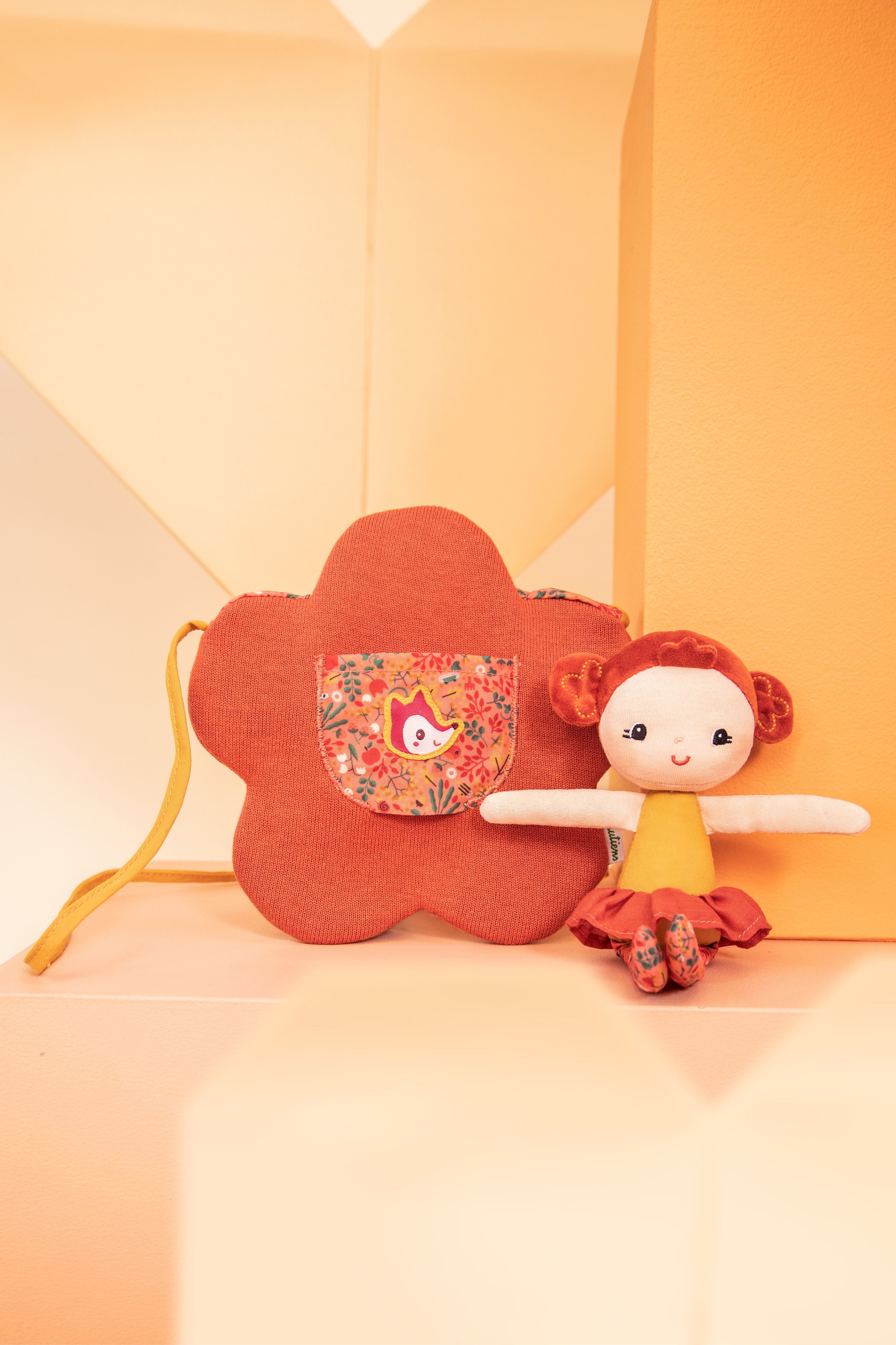 Lilliputiens Adèle doll with flower bag on an orange and peach background