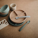 Mushie silicone suction divided plate in Blush styled with baby feeding accessories