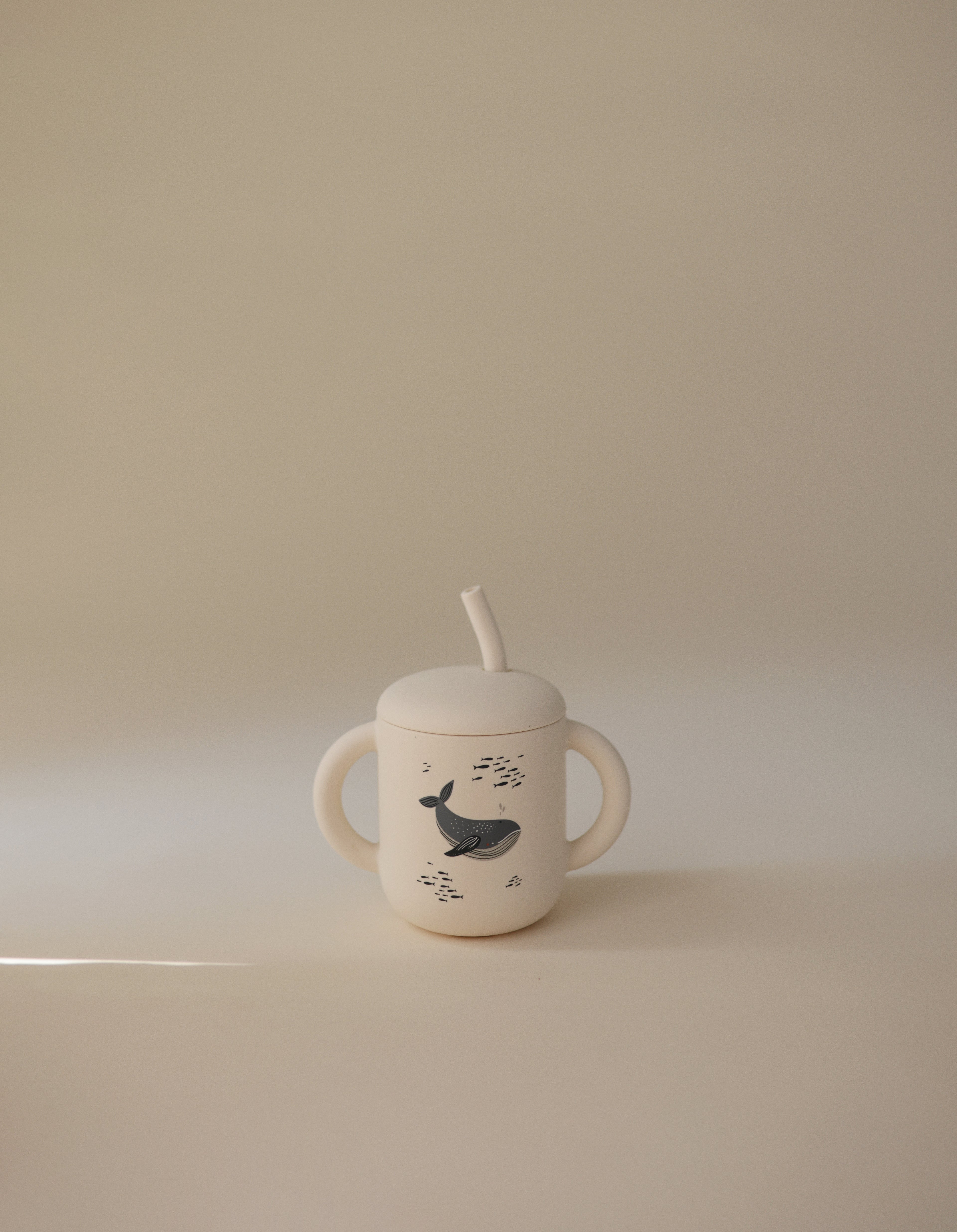 Mushie training cup with straw in Whales print on a beige background