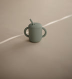 Mushie training cup with straw in Cambridge blue on a beige background