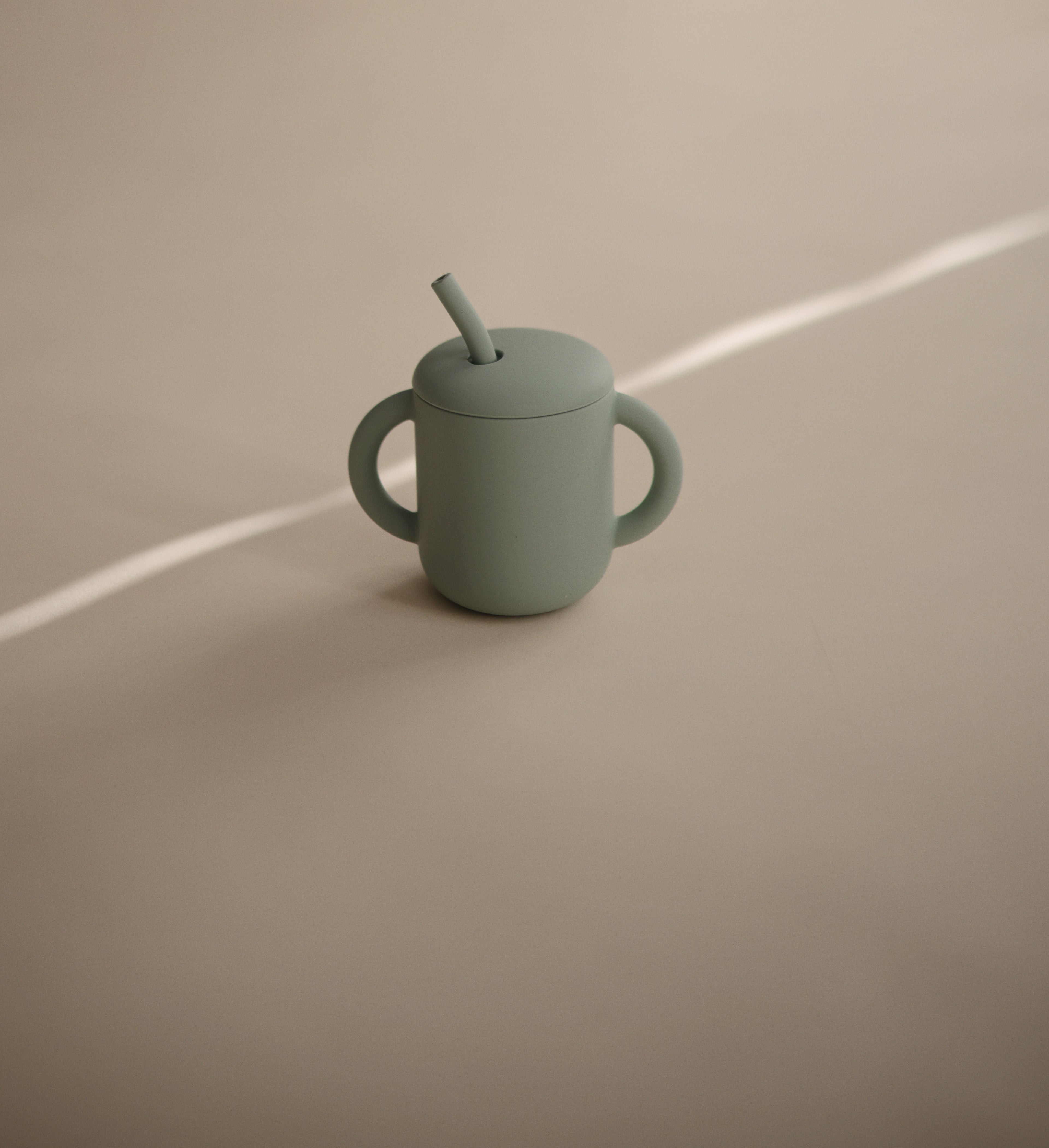 Mushie training cup with straw in Cambridge blue on a beige background