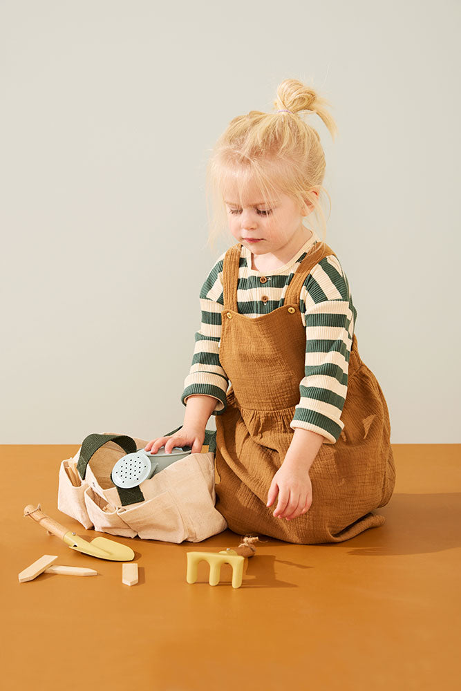 Child playing with Accessories of a Kid's Concept gardening tool set for kids on a brown surface