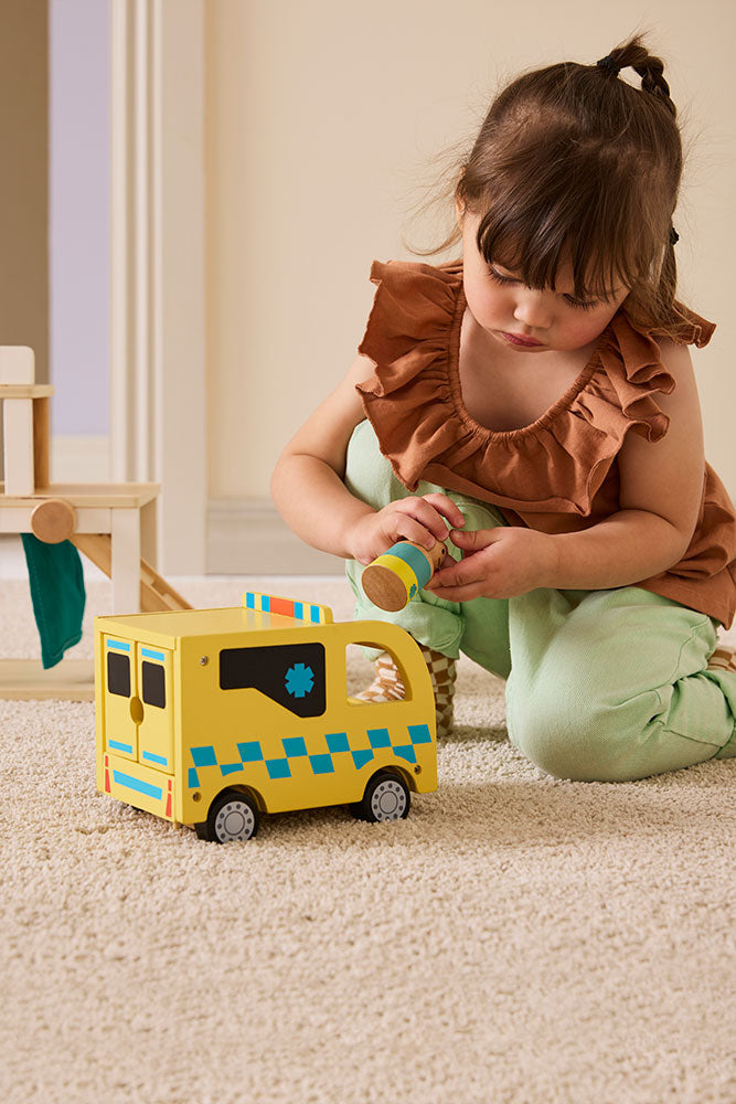 Child playing with a Kids Concept wooden toy ambulance on a carpeted floor