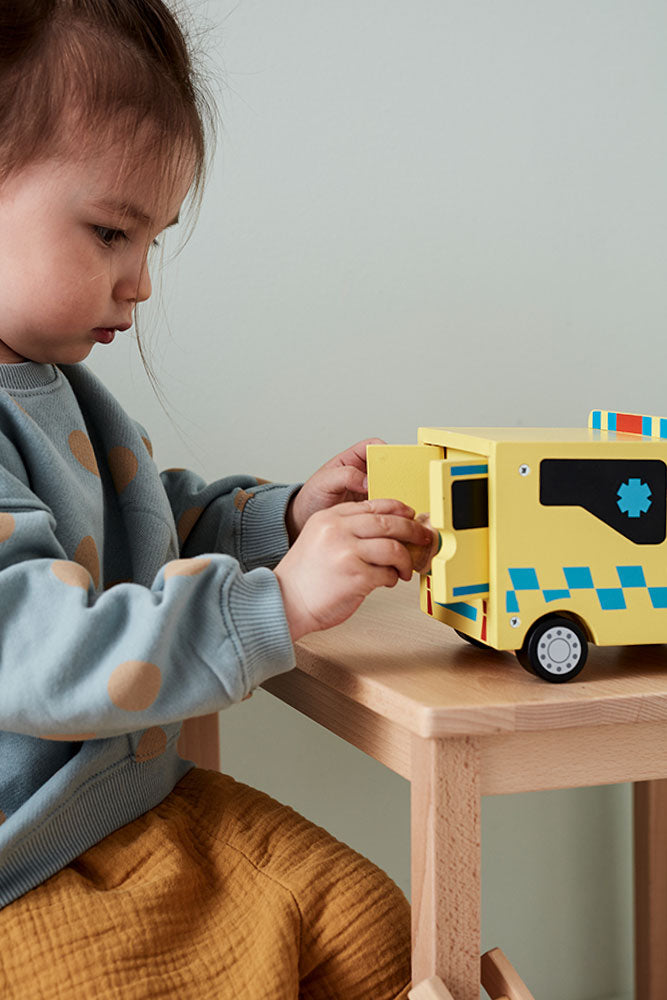 Child playing with a Kids Concept wooden toy ambulance on a wooden table