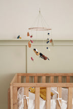 Wooden crib with a Kid's Concept baby mobile hanging above it against a plain wall