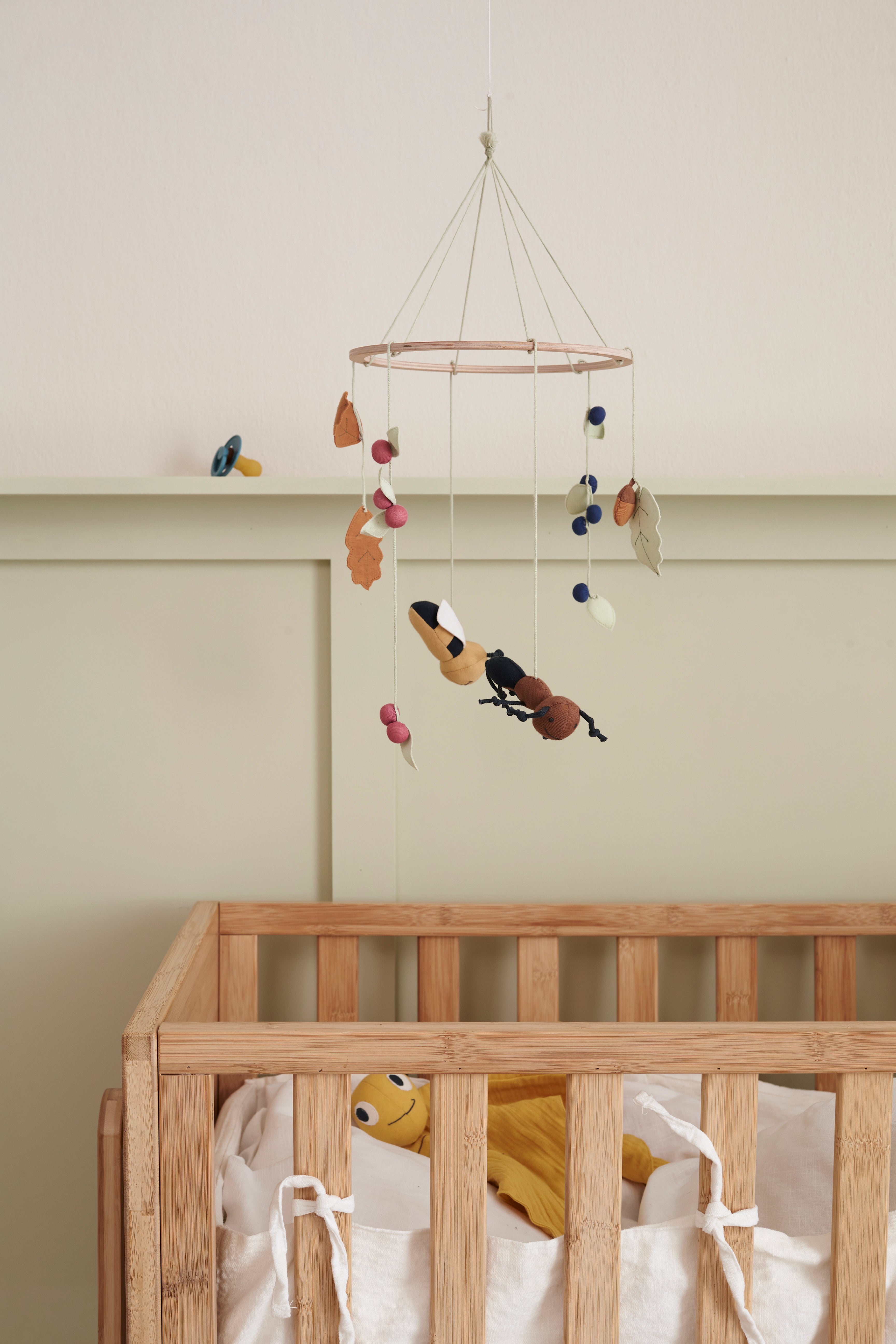 Wooden crib with a Kid's Concept baby mobile hanging above it against a plain wall