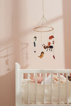 Kids Concept baby mobile hanging above a white crib in a pink nursery with a baby lying in the crib