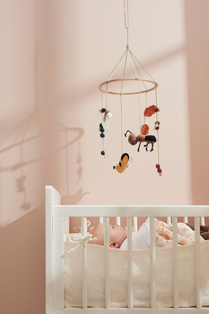 Kids Concept baby mobile hanging above a white crib in a pink nursery with a baby lying in the crib