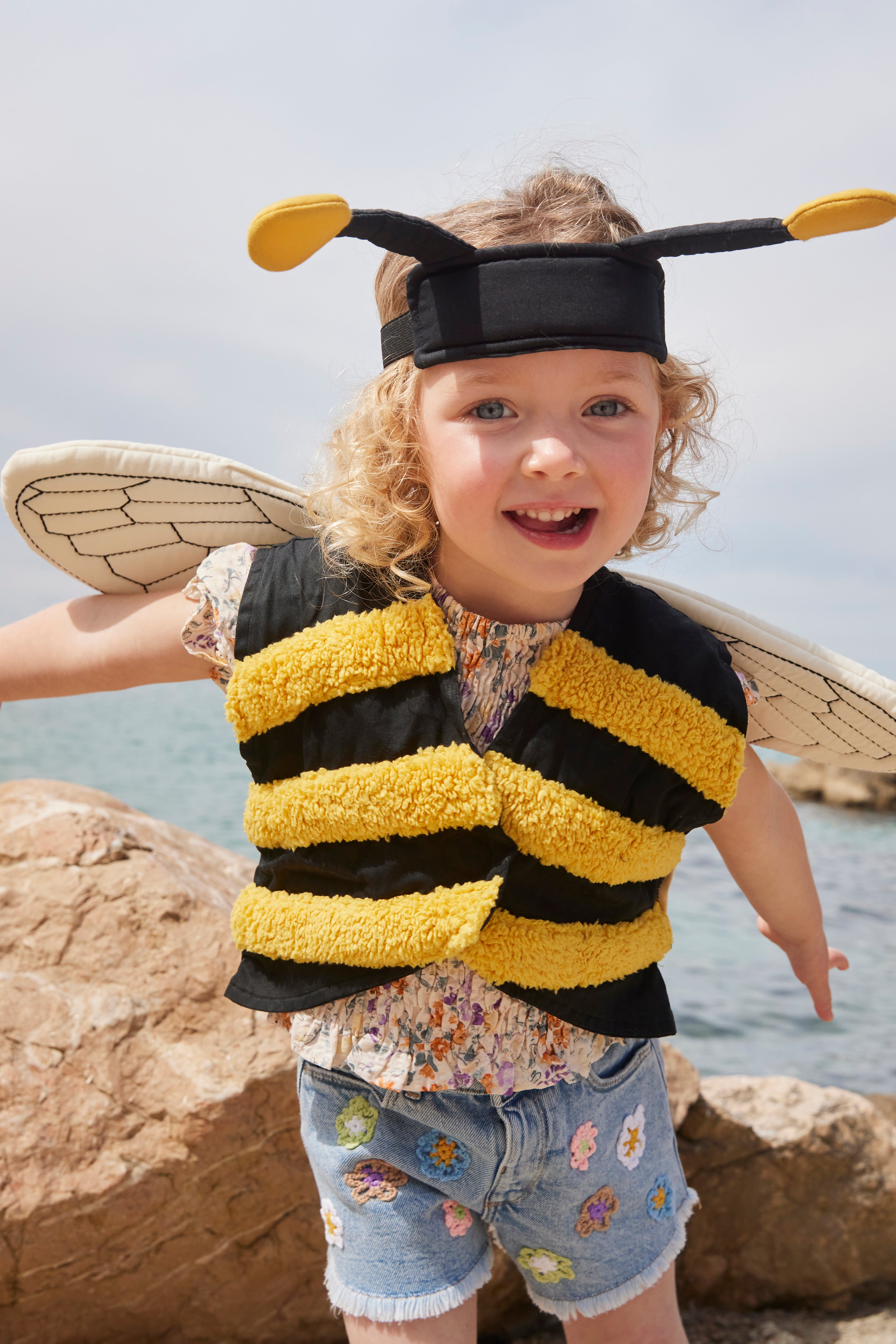 Child wearing a Kid's Concept bumblebee dress-up costume by a body of water