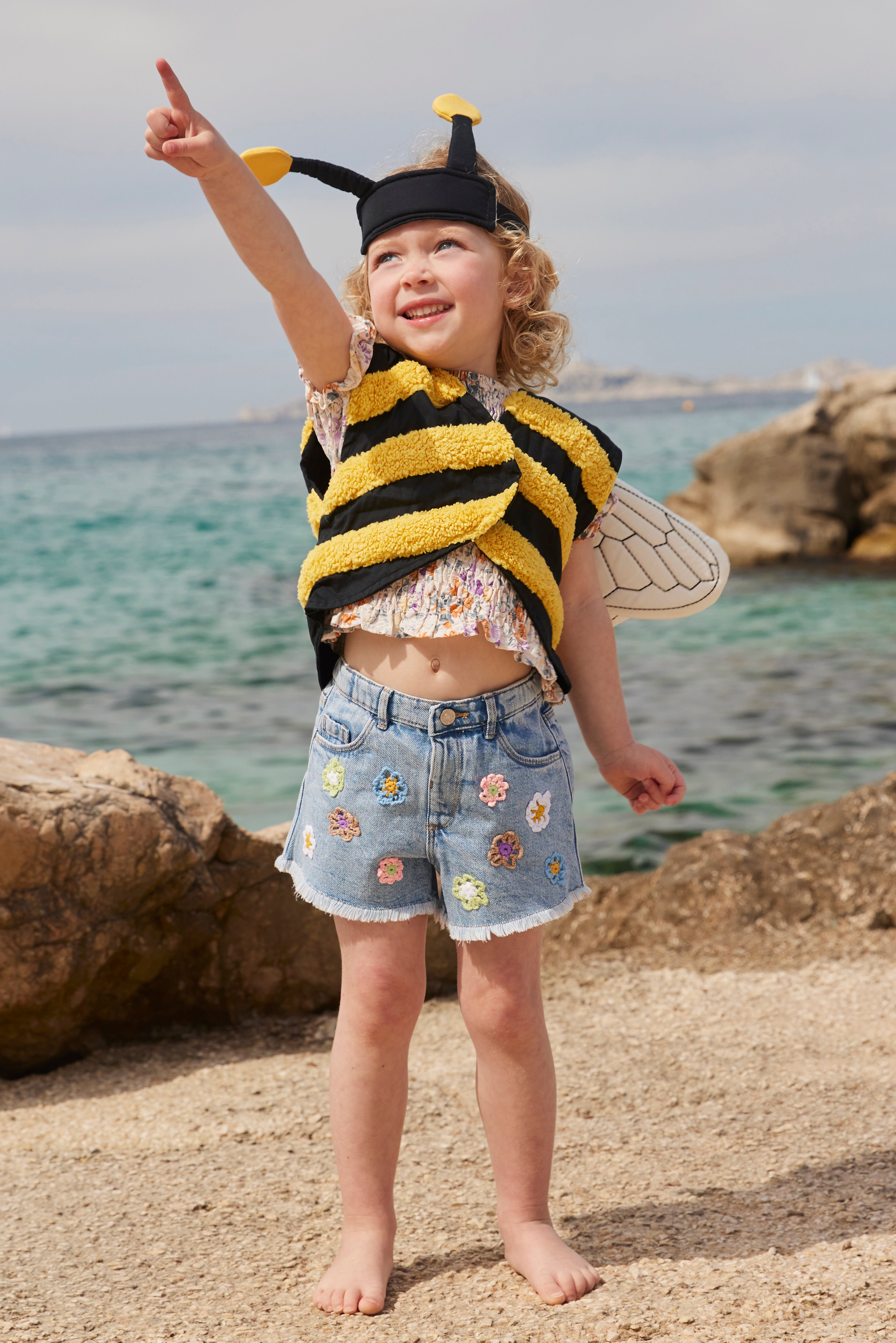 Child in a Kid's Concept bumblebee dress-up costume standing on a rocky beach with ocean in the background