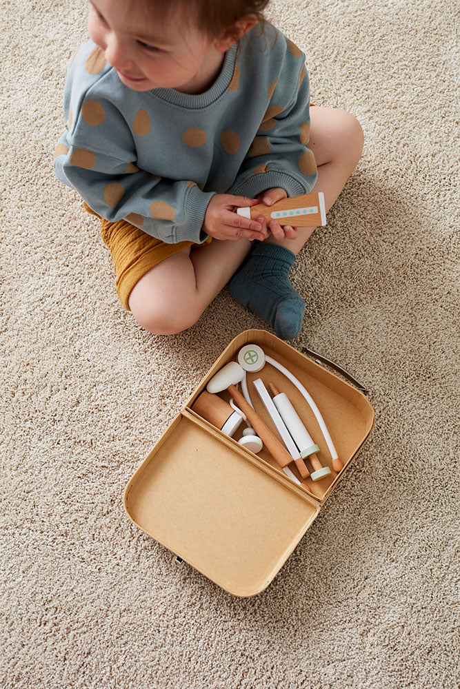 Child sitting on a carpet with a Kid's Concept doctor’s case play set in nature