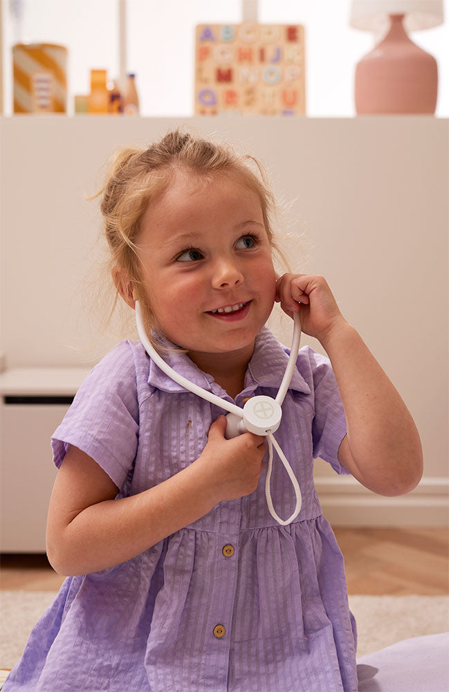 Child in a purple dress playing with a Kid's Concept doctor’s case play set in nature in a home setting