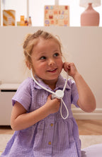 Child in a purple dress playing with a Kid's Concept doctor’s case play set in white in a home setting