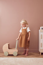 Child playing with a Front view of a Kid's Concept doll pram against a pink wall
