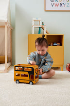 Child playing with a Kid's Concept wooden double decker bus toy in a room with a yellow cabinet and alphabet poster
