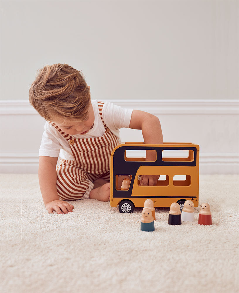 Child playing with a Kid's Concept wooden double decker bus toy on a carpeted floor