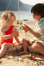 Two children playing with Kids Concept wooden drink play set on a sandy beach
