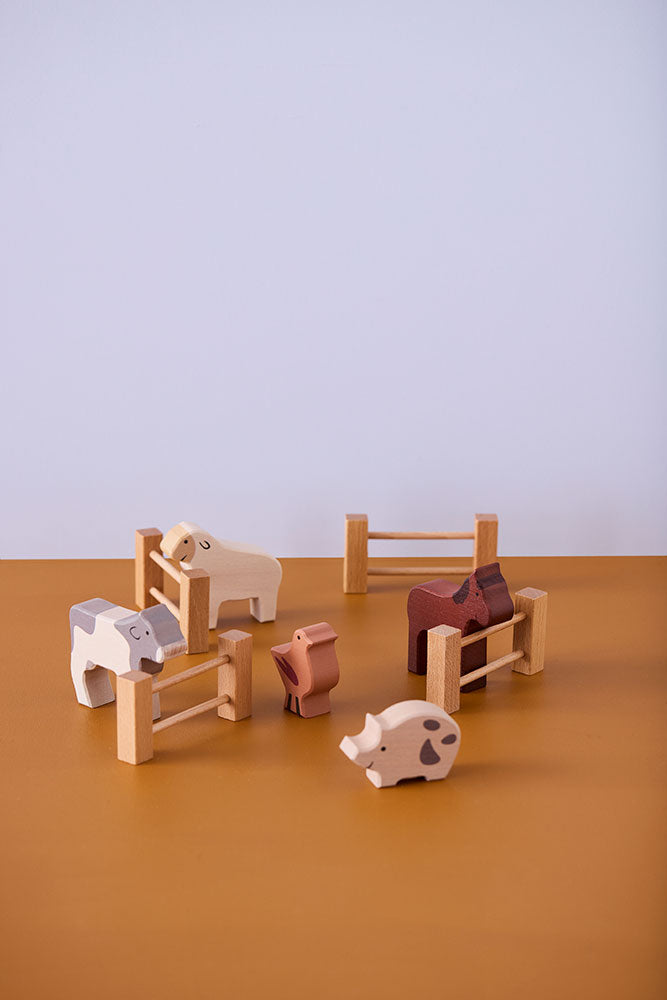 Kid's Concept wooden farm animals set on a brown surface with a light purple background