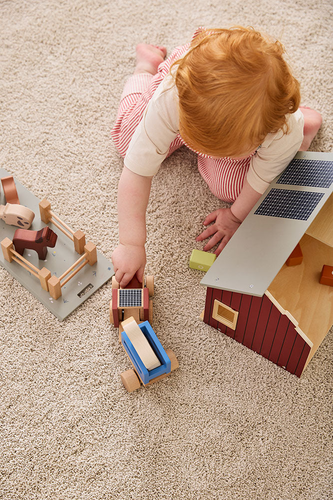 Child playing with Kid's Concept wooden farmhouse toy on a carpeted floor