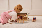 Child playing with Kid's Concept wooden farmhouse toy on a carpeted floor