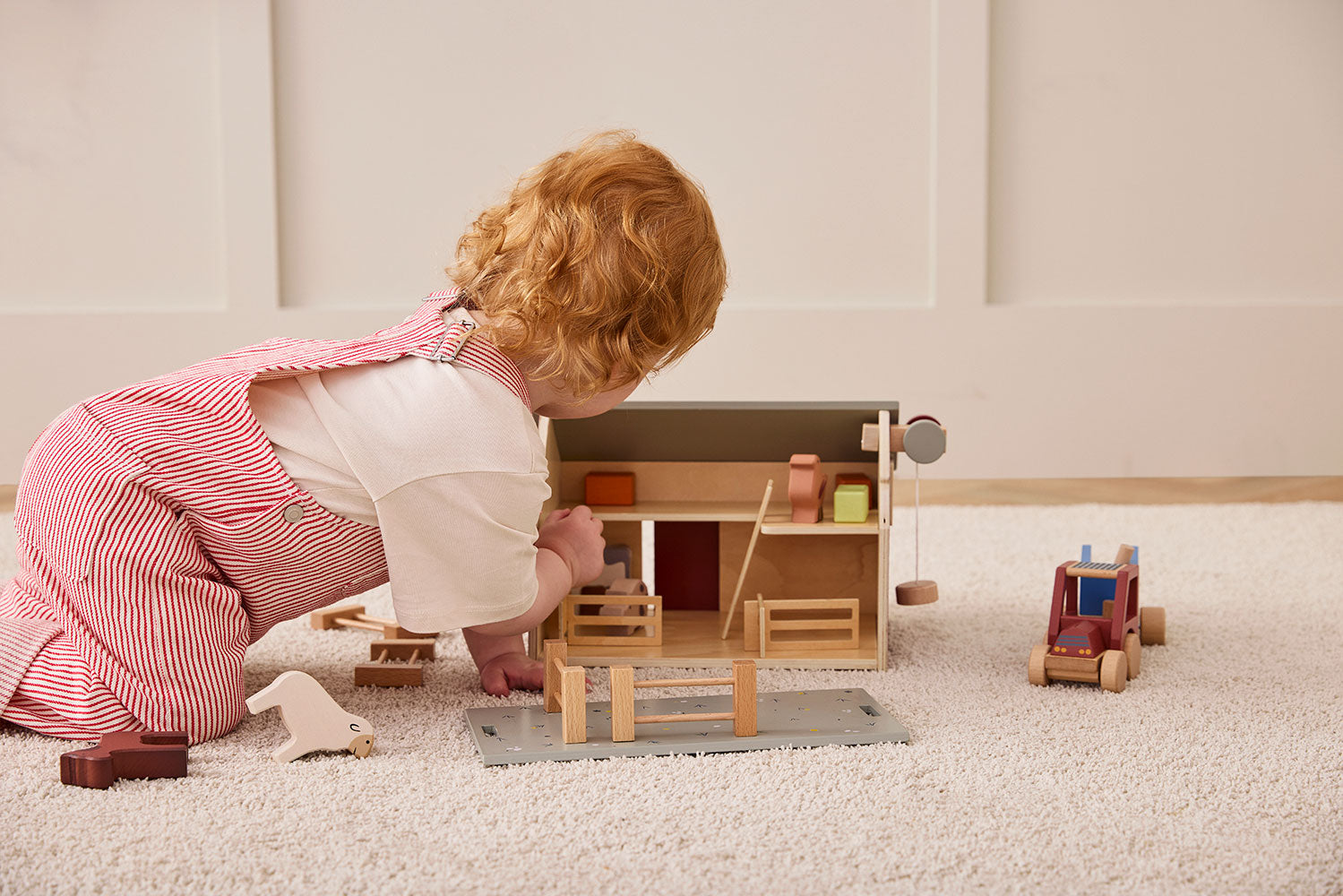 Child playing with Kid's Concept wooden farmhouse toy on a carpeted floor