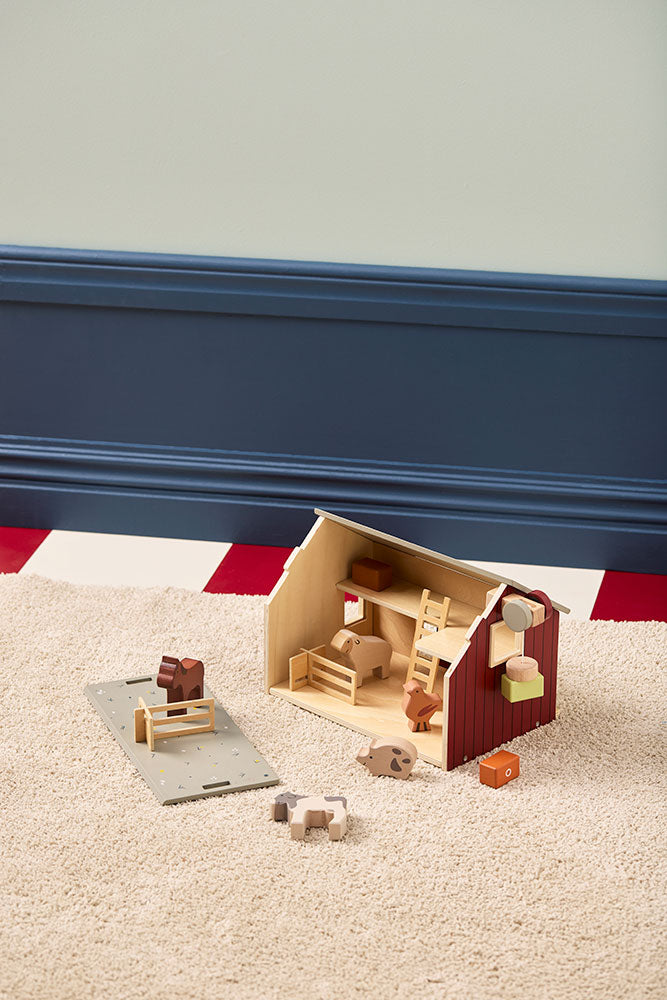 Kid's Concept wooden farmhouse toy on a carpet against a blue background