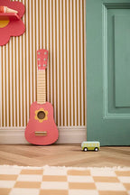 Kid's Concept wooden toy guitar against a striped wall with a green door and checkered floor